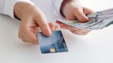 A woman's hand holds a cash back credit and U.S. hundred dollar bills.