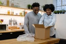 A couple opens a large package in their kitchen