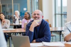 Man sits at a desk in front of his laptop in a classroom.