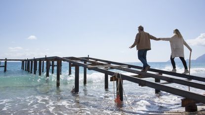 A couple balance on the frame of a pier over the water.