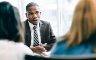 A financial adviser in a suit talks to clients in an office.