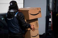 An Amazon delivery driver carries boxes into a van outside of a distribution facility