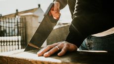 A man uses a hand saw on a piece of wood, only his hands showing.