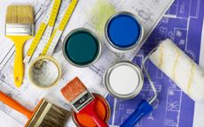 Paint brushes, cans and tape, along with a roller, rest atop blueprints, indicating a remodeling project.