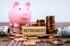 Wooden block with the word "retirement" sits on table with cash, coins and a piggybank.