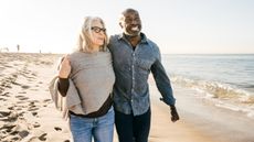 A senior couple walks on the beach arm-in-arm.