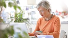 A retired woman works on her laptop at the dining room table.