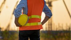 The back view of a construction worker wearing a safety vest and holding a construction helmet