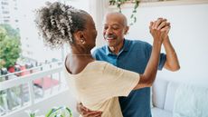 A retired couple dance around their living room together.