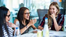 Three businesswomen laugh and smile while sitting at a conference table in an office