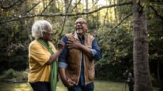 A retired couple laugh together as they hike through a wooded area.